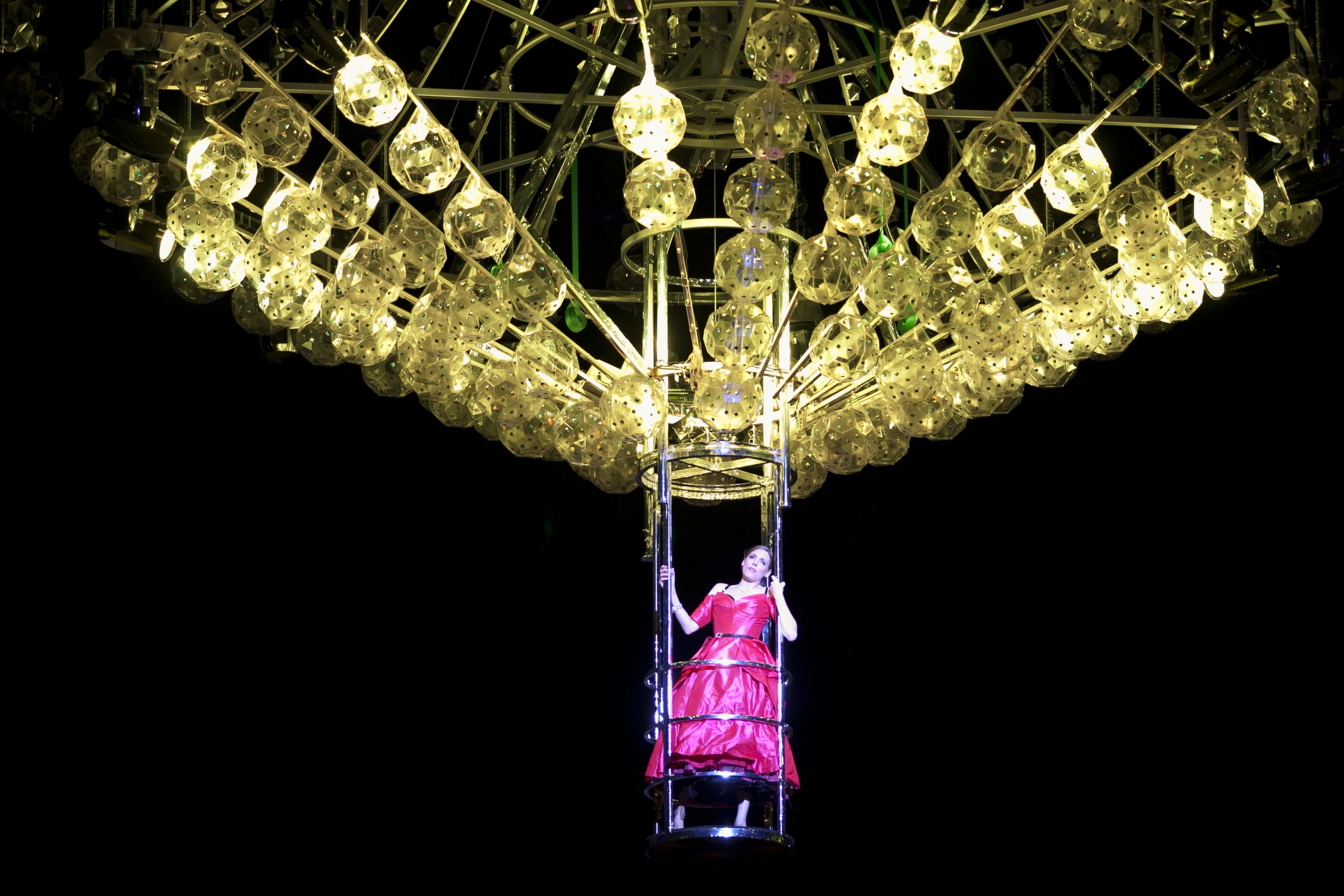 Woman hanging on to giant crystal chandelier in Opera Australia's production of La Traviata on Sydney Harbour in 2012 