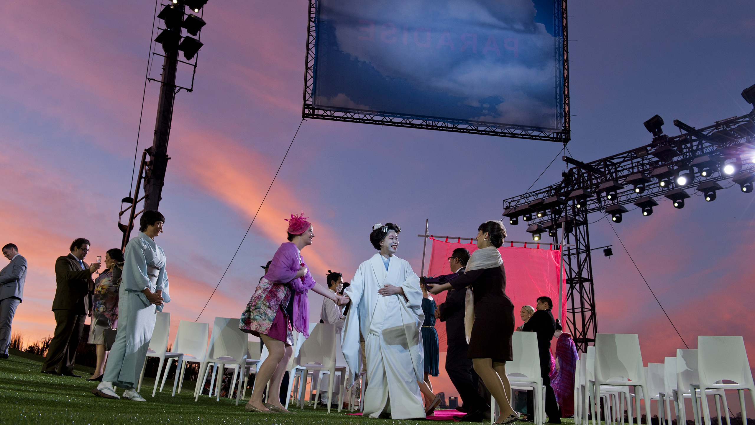A singer plays Cio-Cio-San in an outdoor performance of Madama Butterfly, with a blue and pink sky in the background.