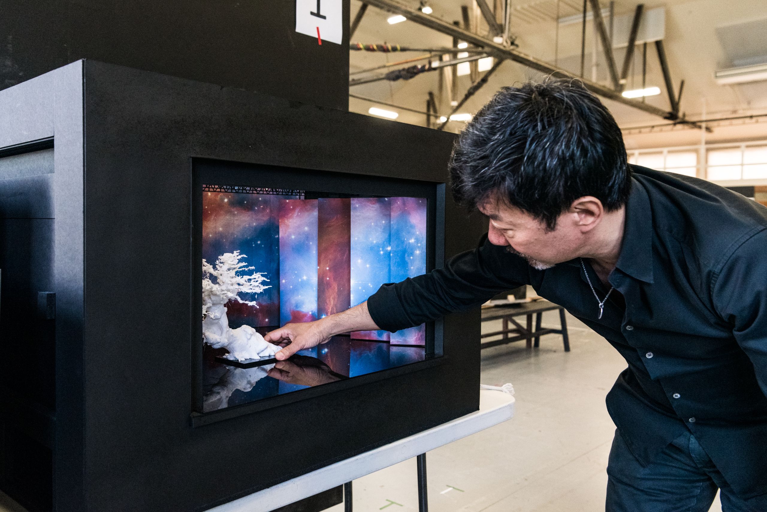 Director Chen Shi-Zheng moves a small white bonsai tree inside a set model box using his hand.