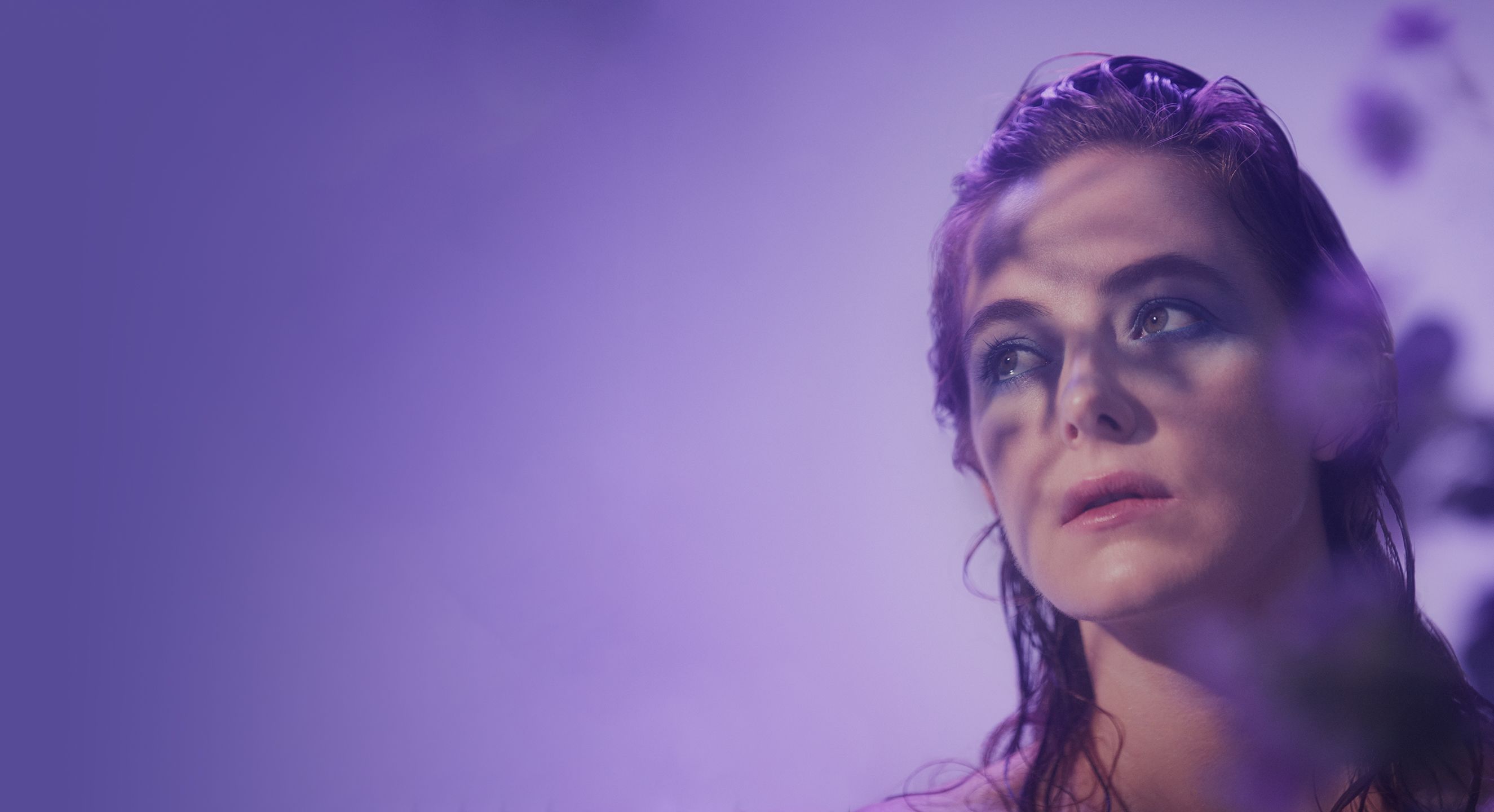 A woman with wet hair and pale makeup, against a purple background.