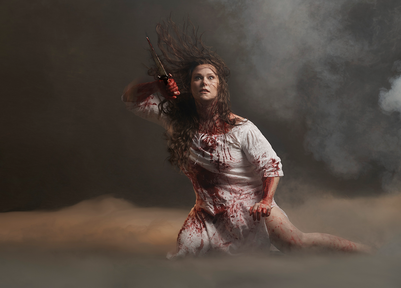 Opera singer Jessica Pratt holds a knife, wearing a white dress and covered in blood.