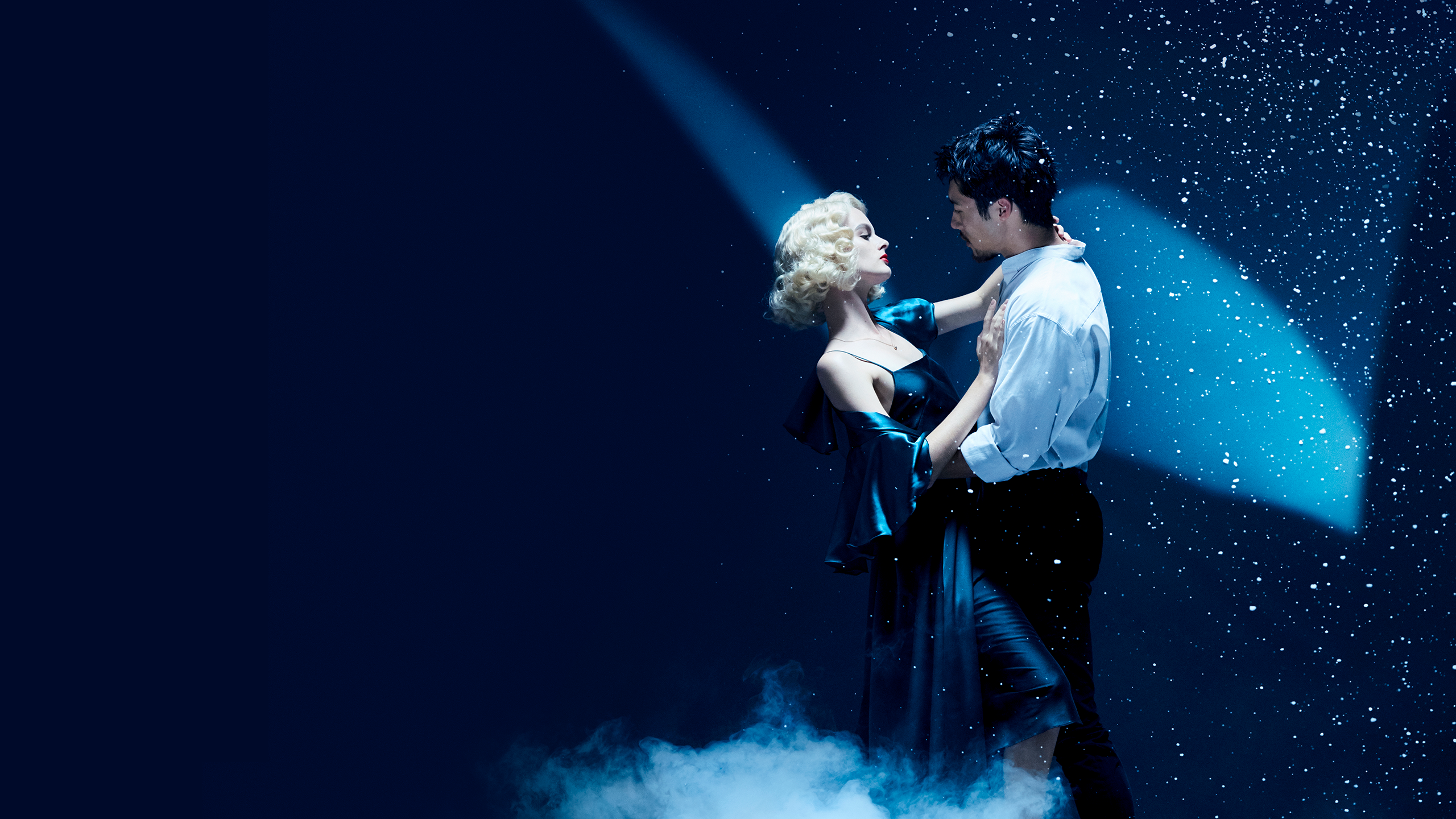 A young man and woman embrace in front of the Sydney Opera House sails as snow falls down.