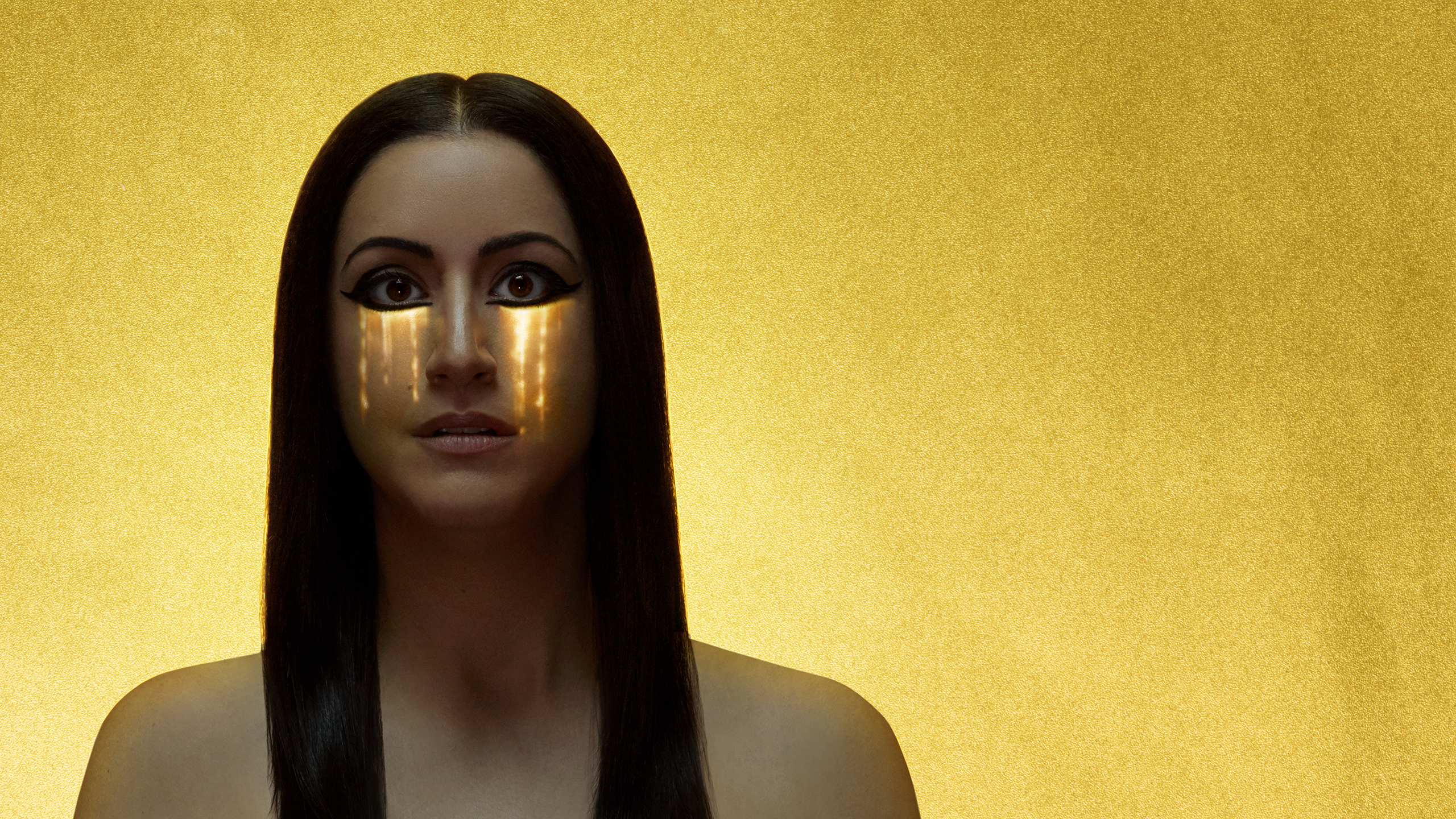 A woman with long, straight black hair stares straight ahead, while golden teardrops fall down her face.
