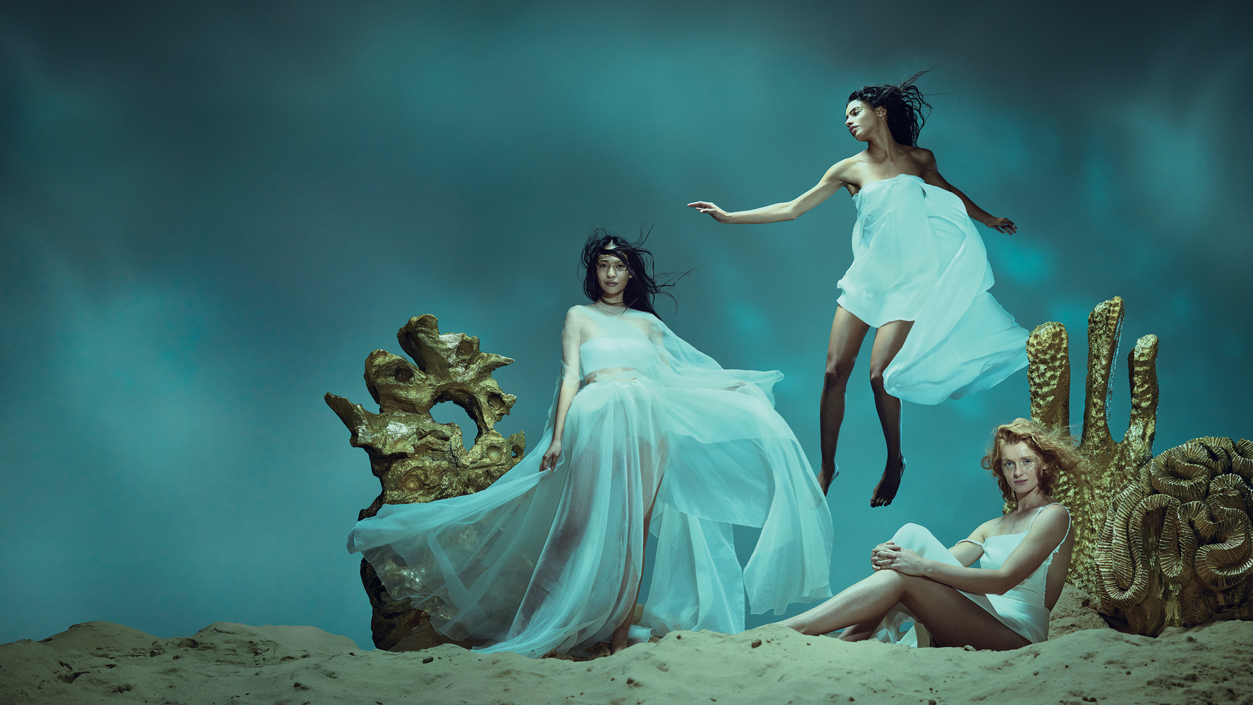 A group of three woman in long white flowing gowns, under water.