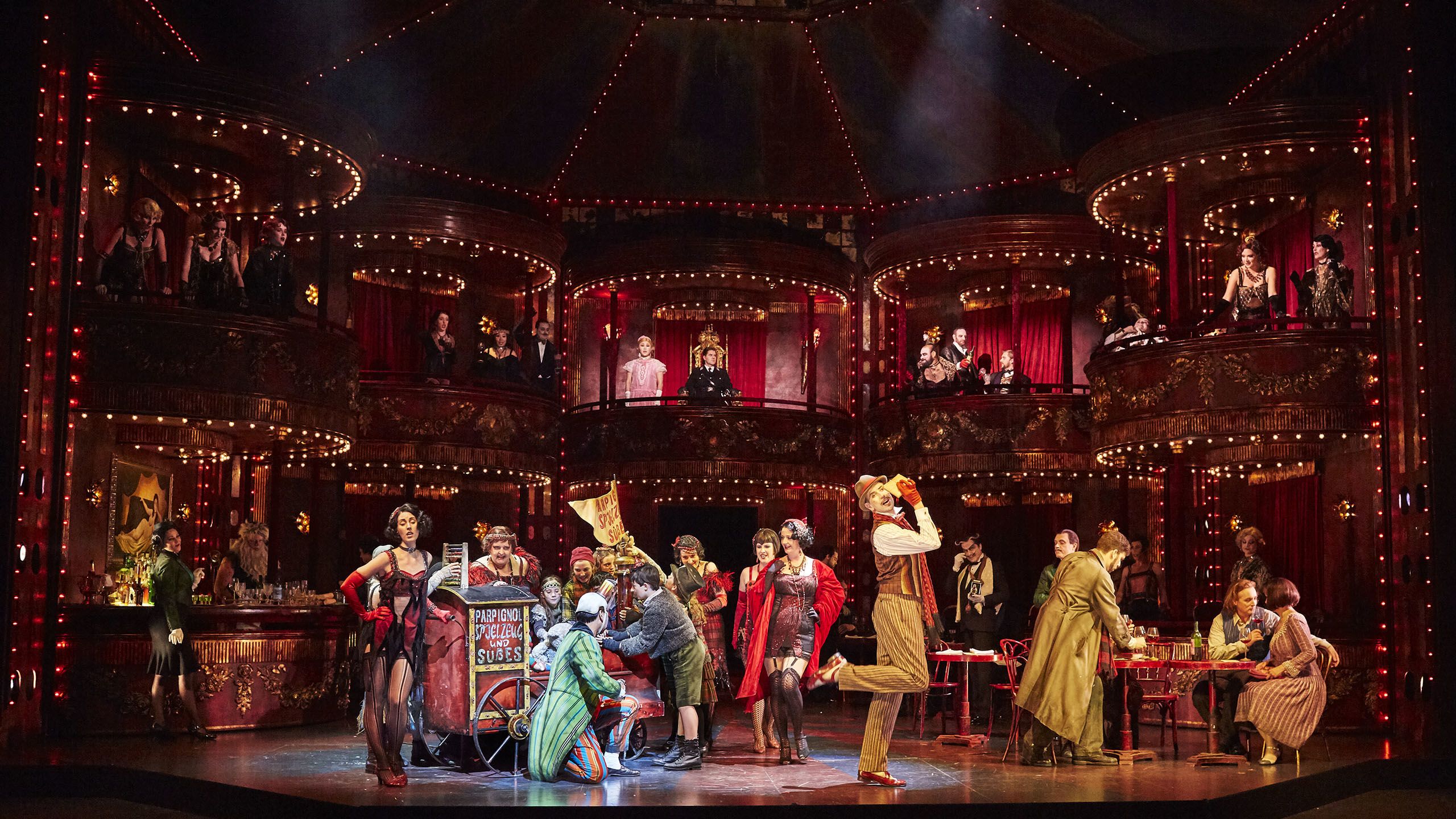 a scene in the opera la boheme with singers in colorful costumes and a set with glamorous red balconies