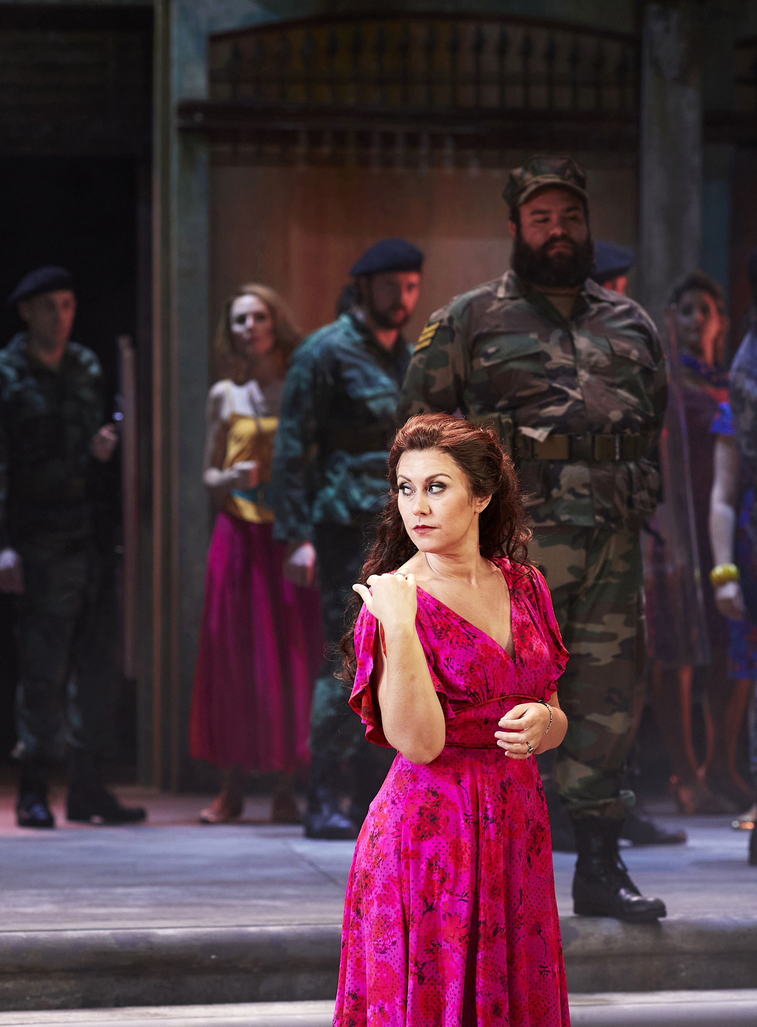 A woman stands in a flowy red dress on stage in a performance of Carmen.