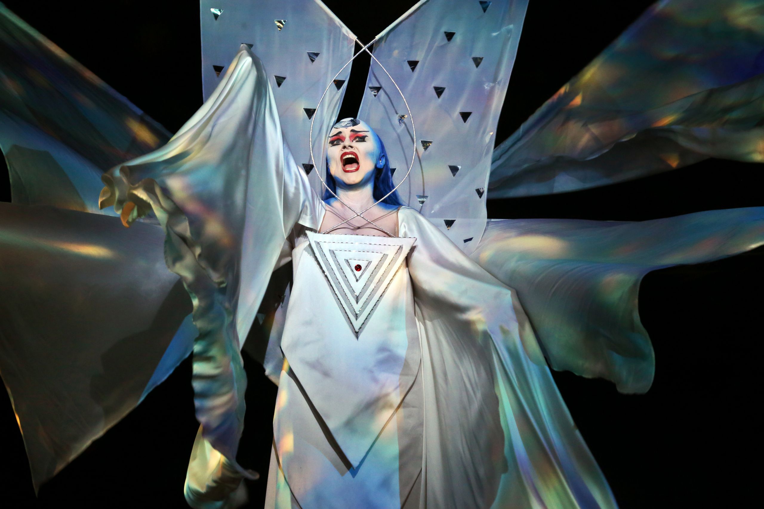 A woman in a fantastical white dress with colourful stage makeup sings in a performance of The Magic Flute.