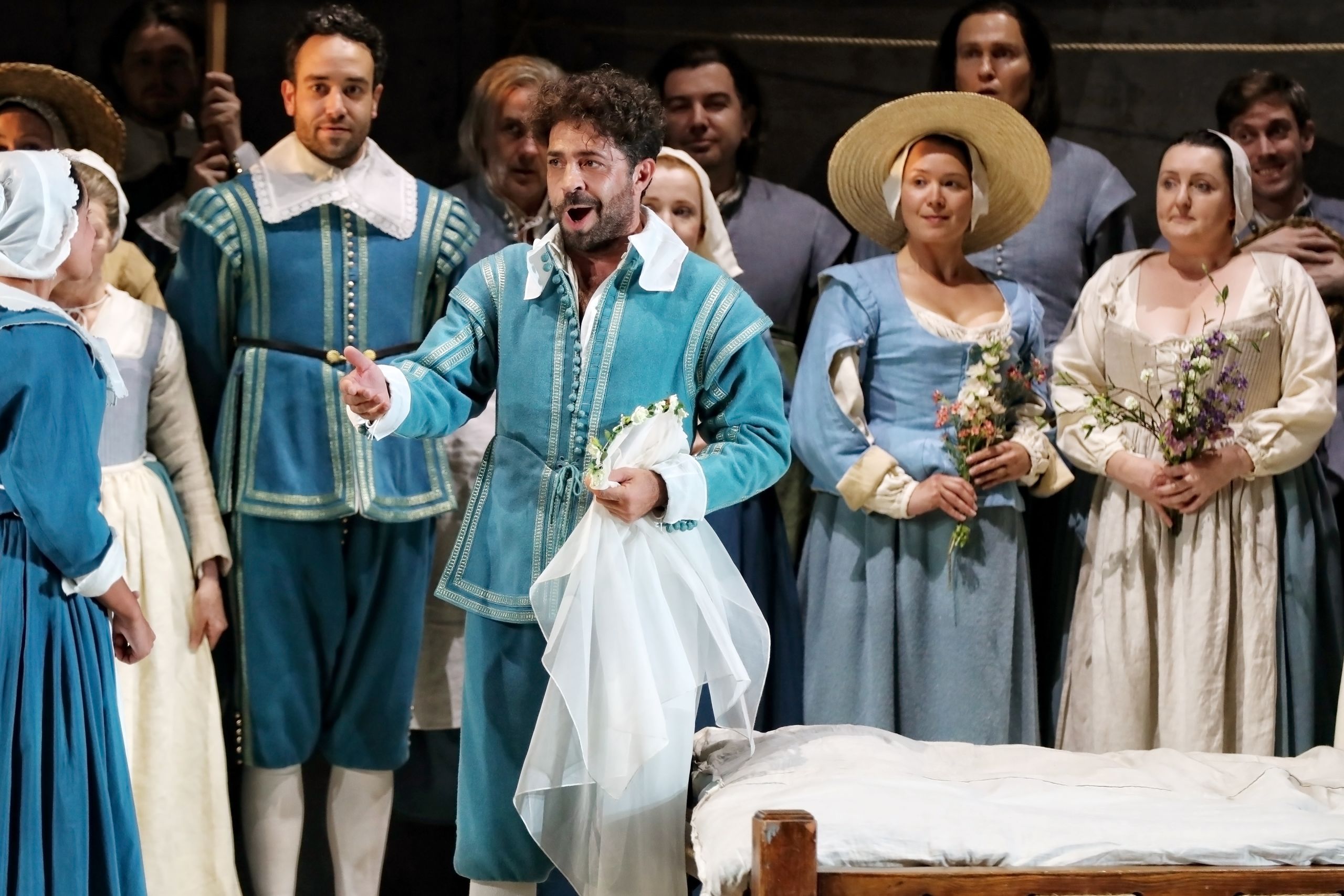 A man in a 16th-century blue suit stands on stage reaching his hand out to a woman in a performance of The Marriage of Figaro.