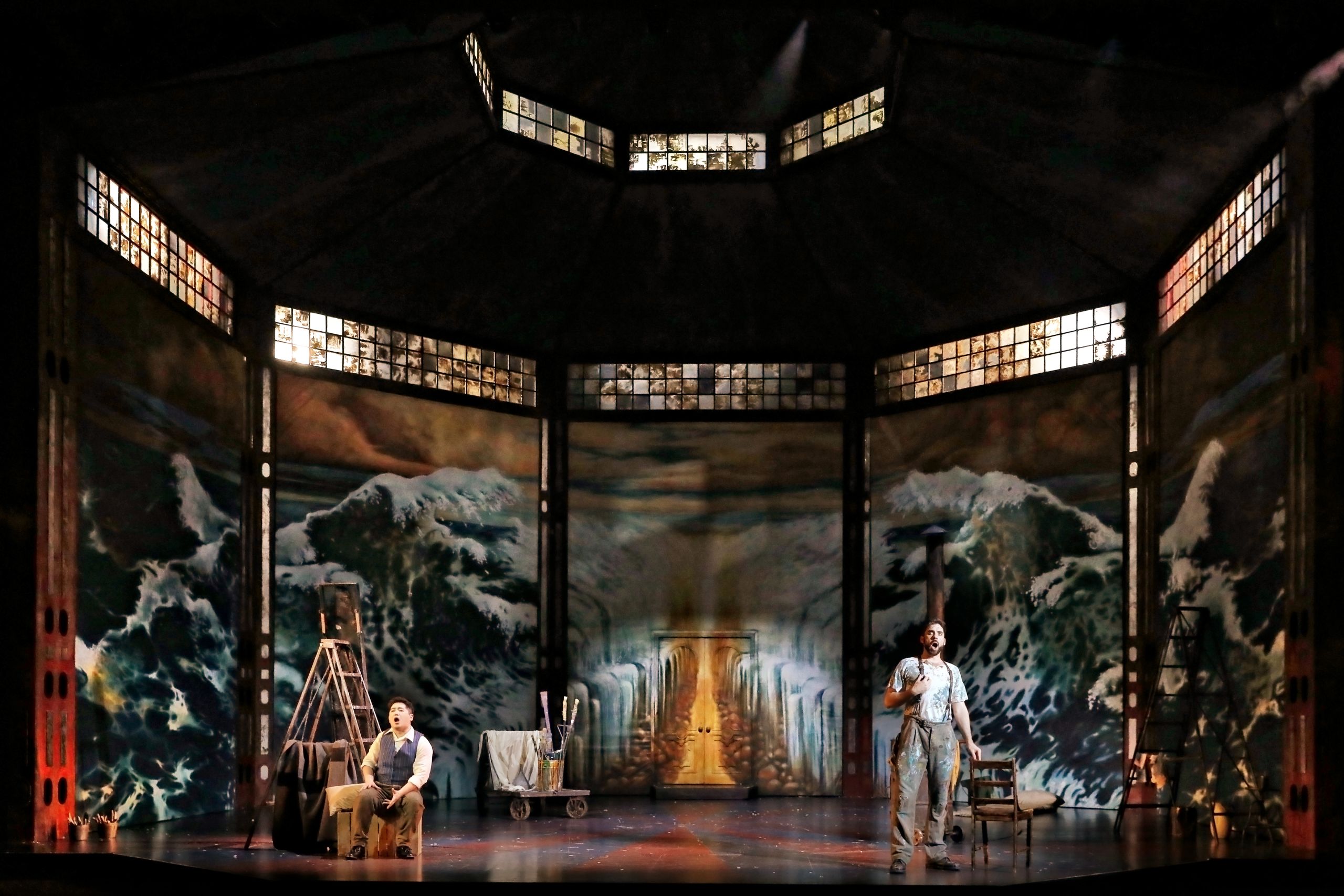 Two men stand inside a lavishly painted loft in a performance of La Boheme.
