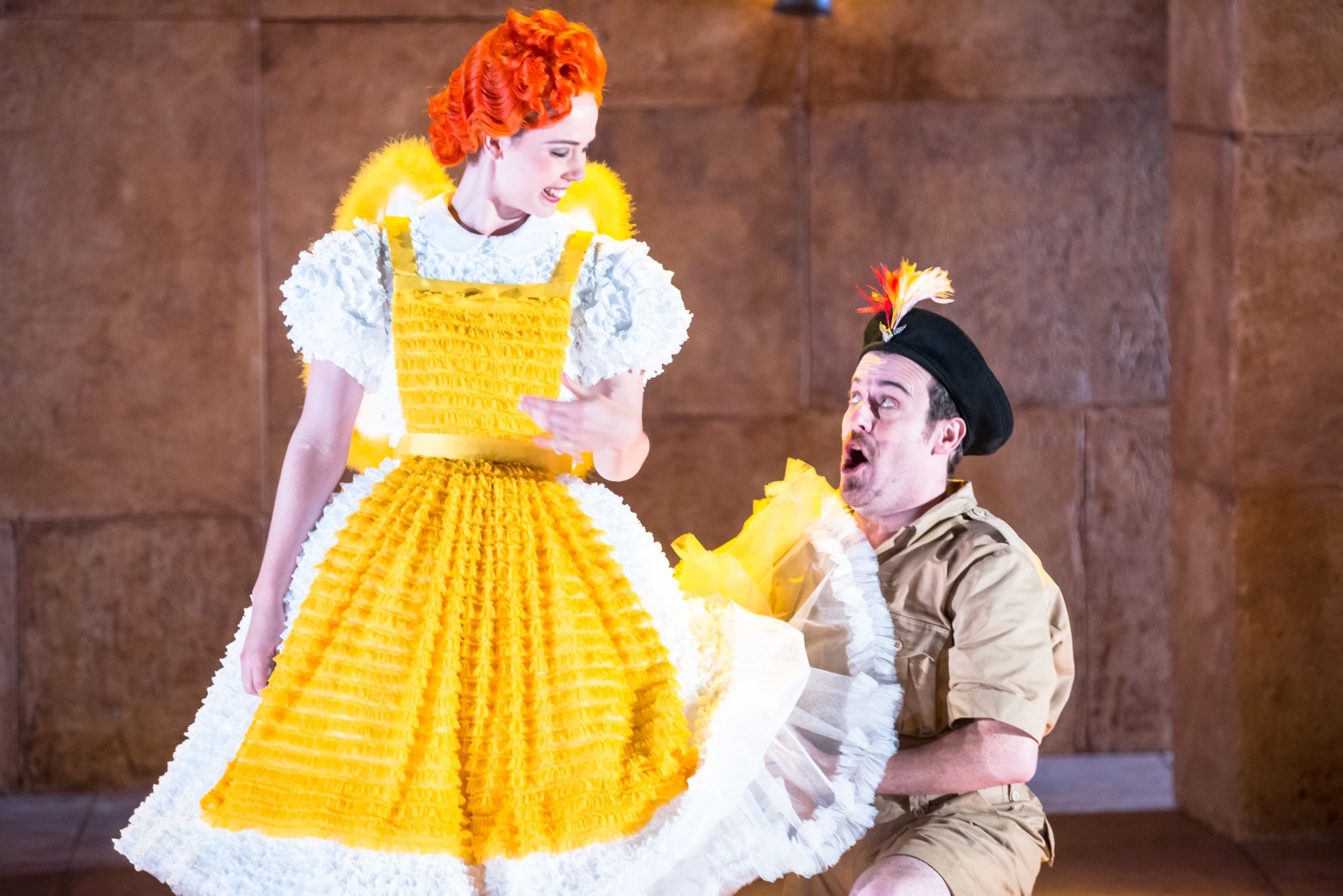 A man kneels before a woman in a bright yellow dress in a performance of The Magic Flute. They are smiling warmly at each other.