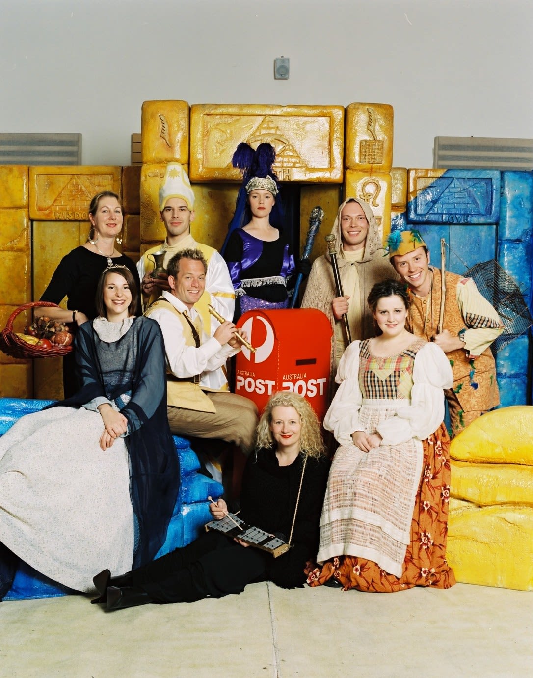 A group of people in various colourful costumes sit around a red Australia Post box.