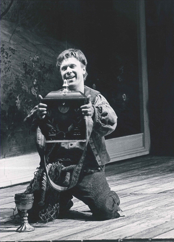 A man kneels, holding a large wireless radio in a performance of The Magic Flute.