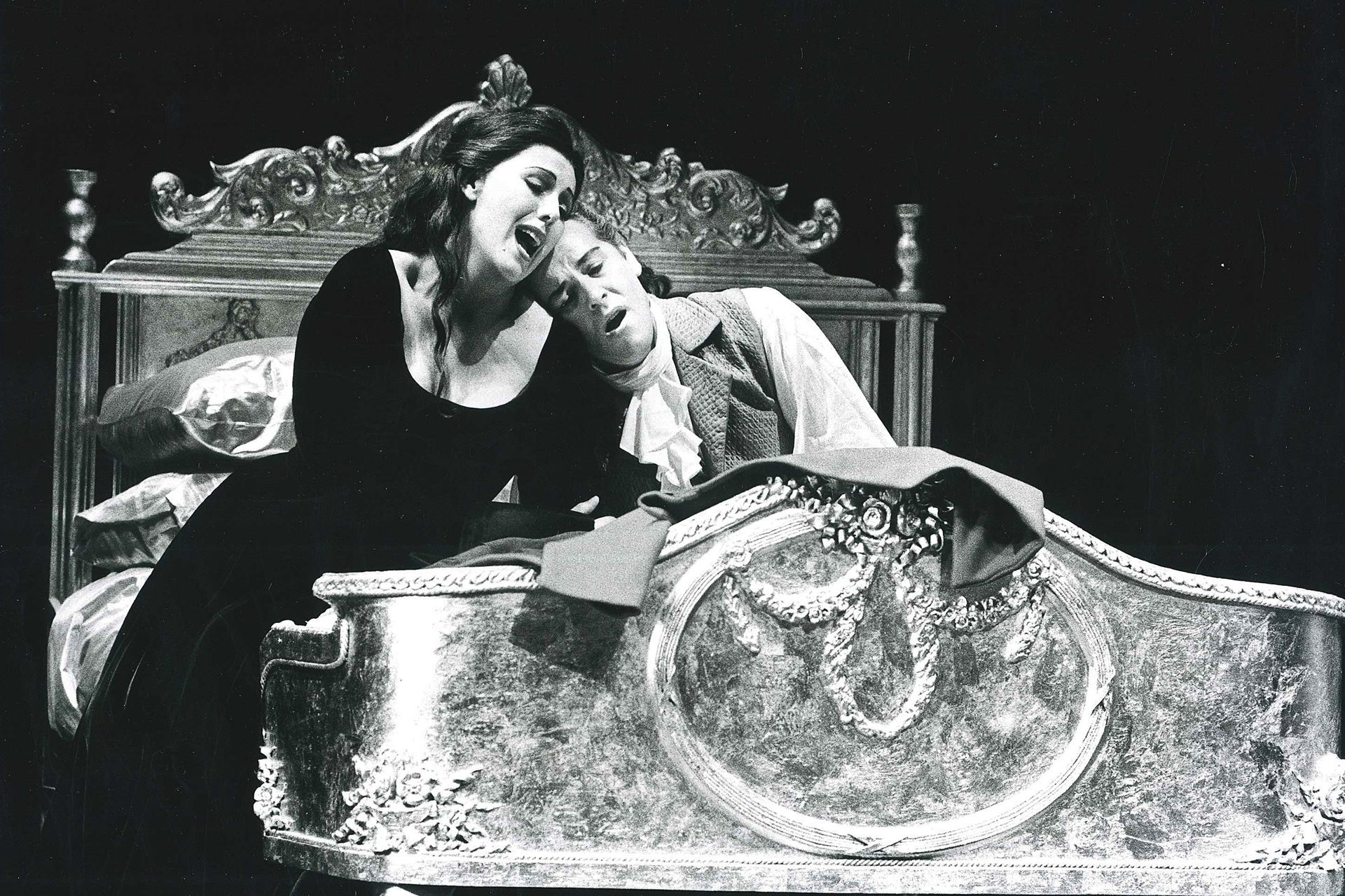 A man and a woman in period costume sit in bed in a performance of The Marriage of Figaro.