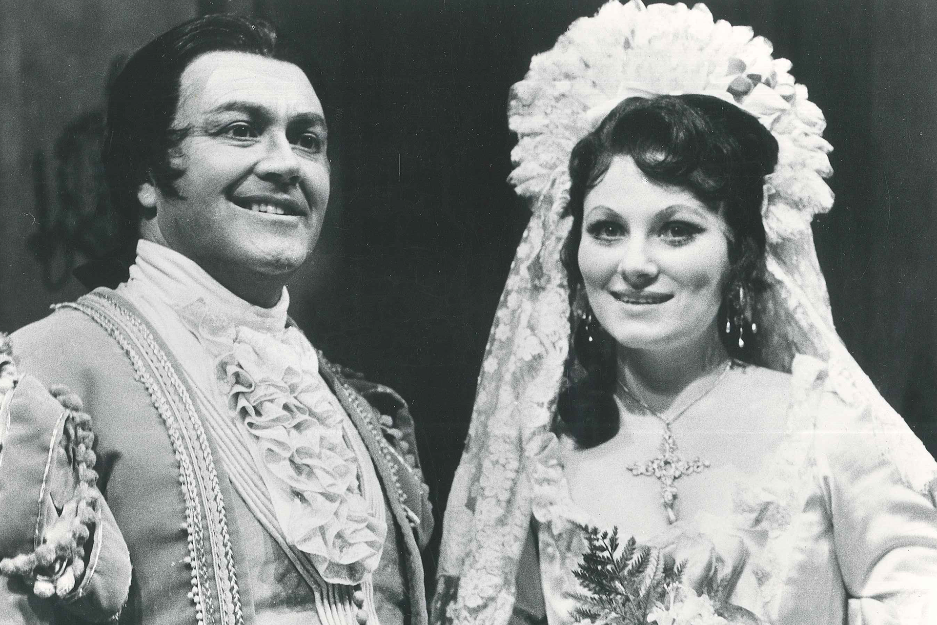 A man and a woman stand in period dress, smiling.