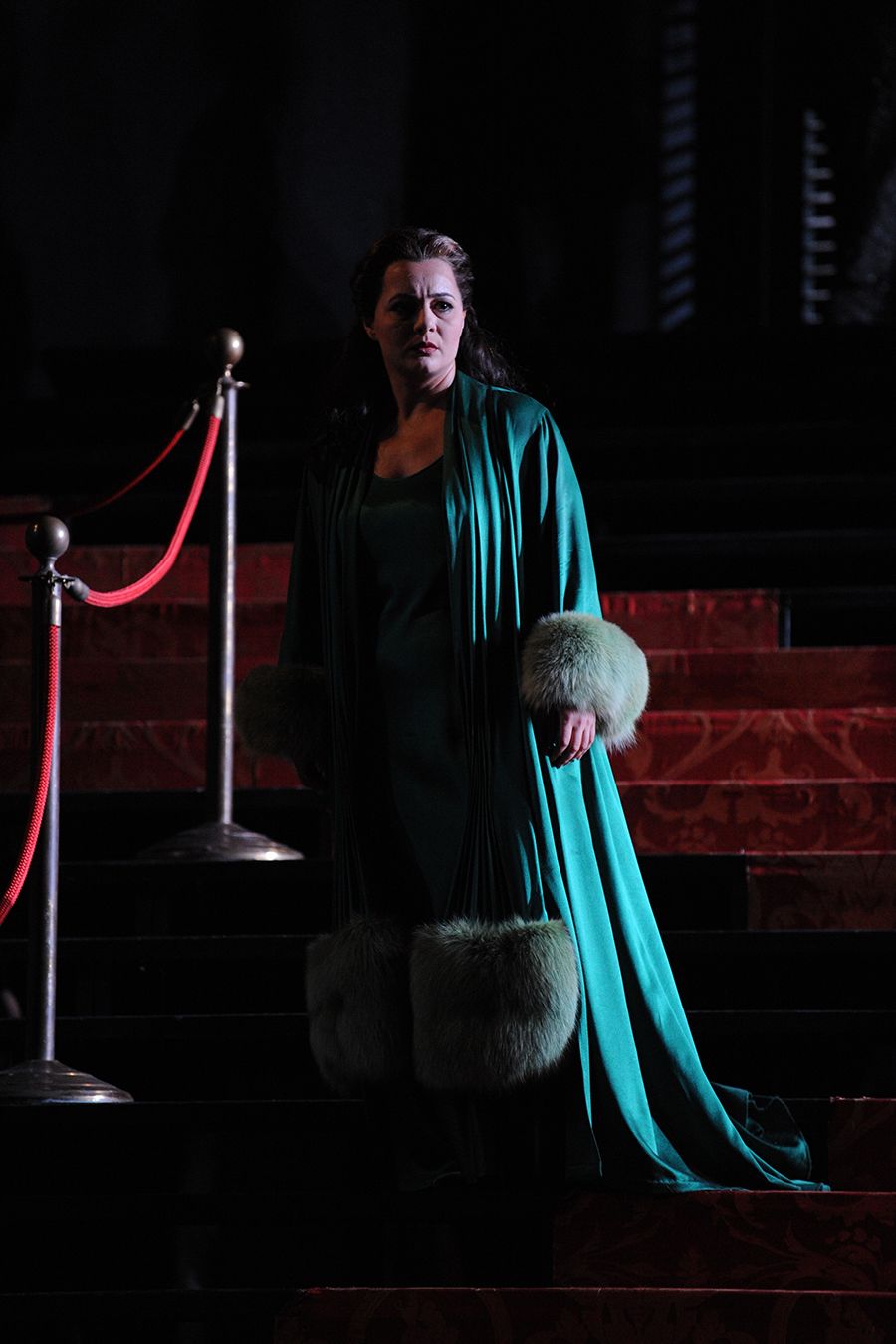 A woman stands on a red staircase in a long green silk gown.