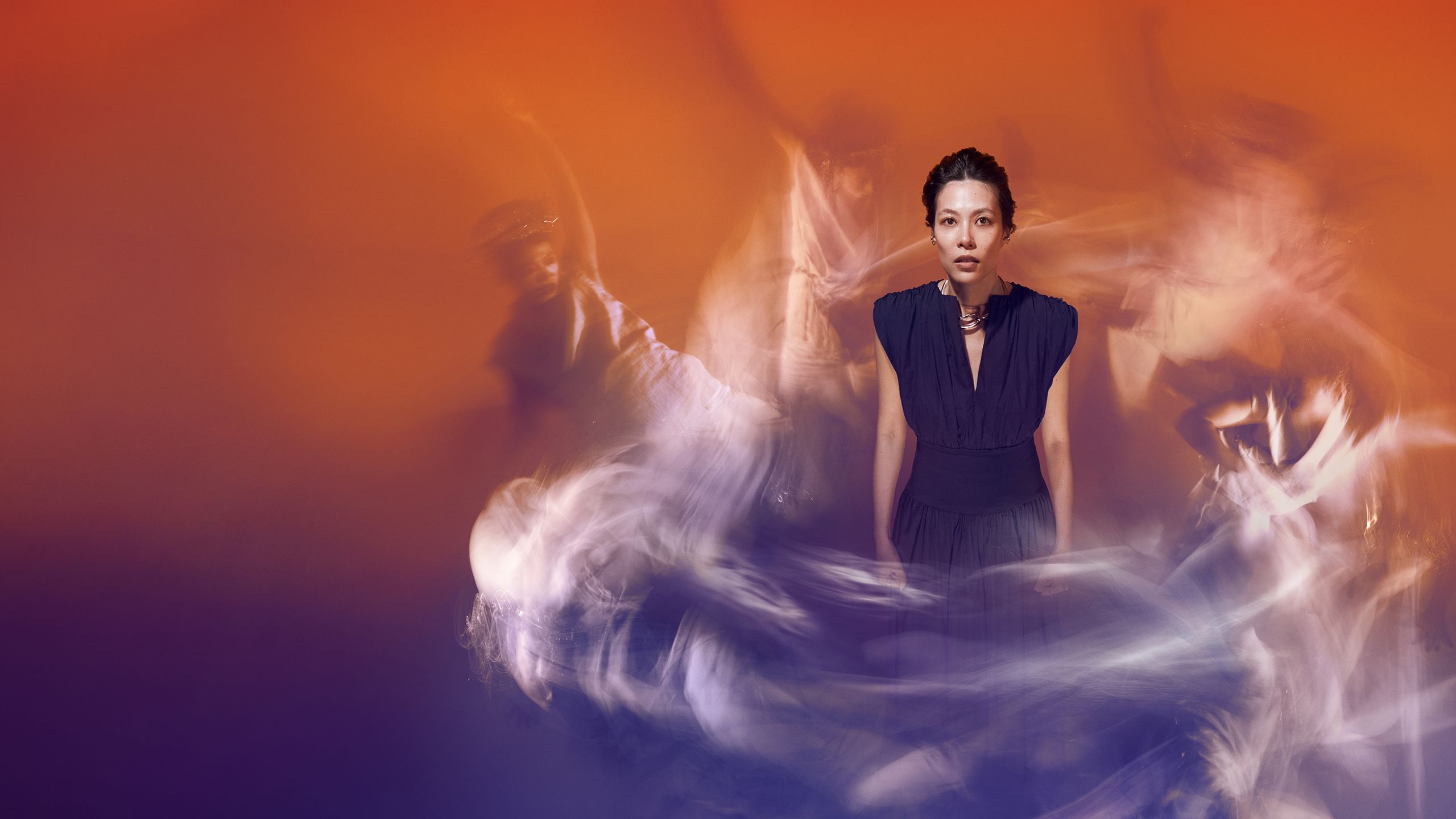 A portrait of a young woman in front of an orange background. She's surrounded by blurred dancers.